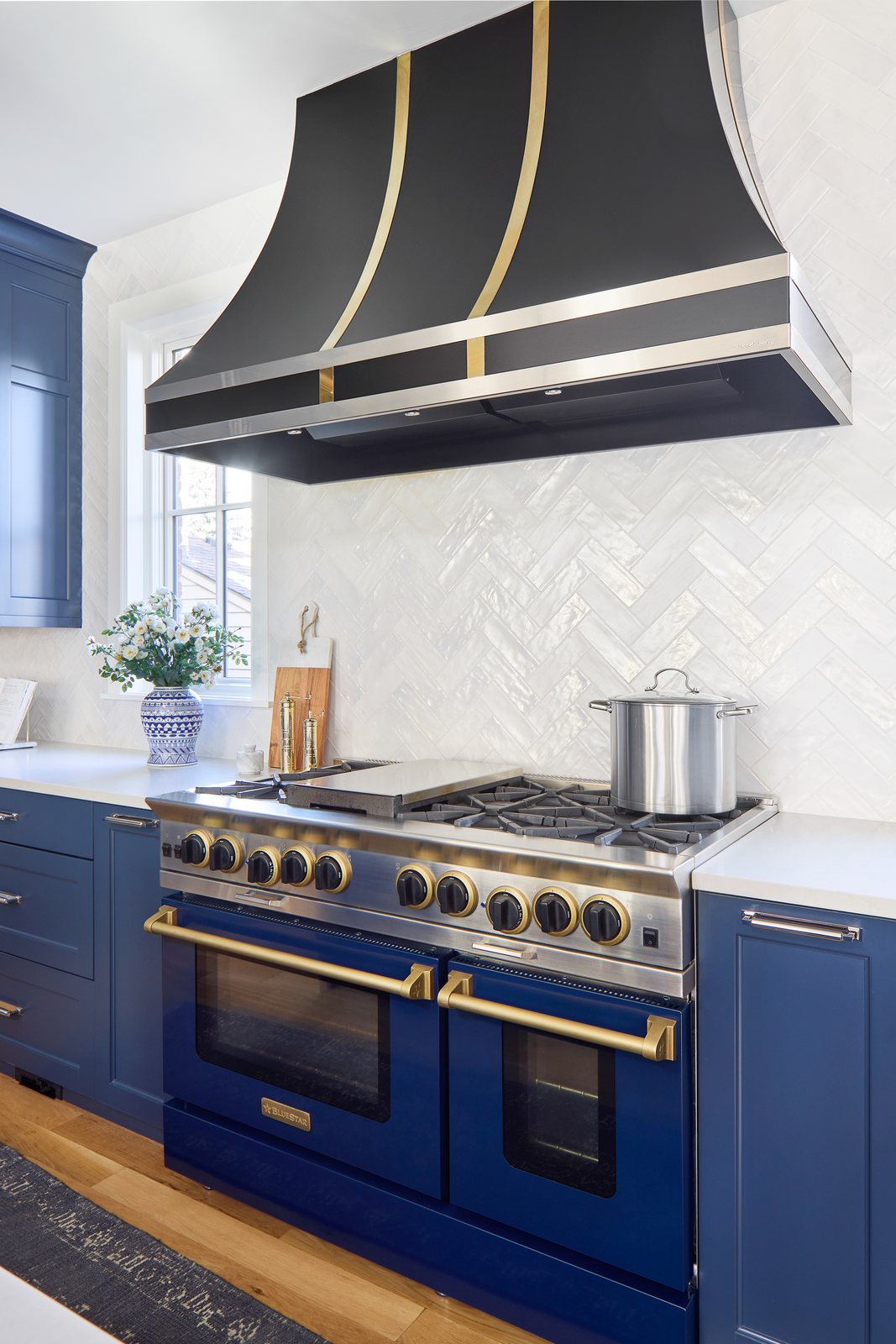 Blue range with brass hardware beneath a black-and-brass hood and herringbone tile in the Bonnie Brae remodel, Denver.