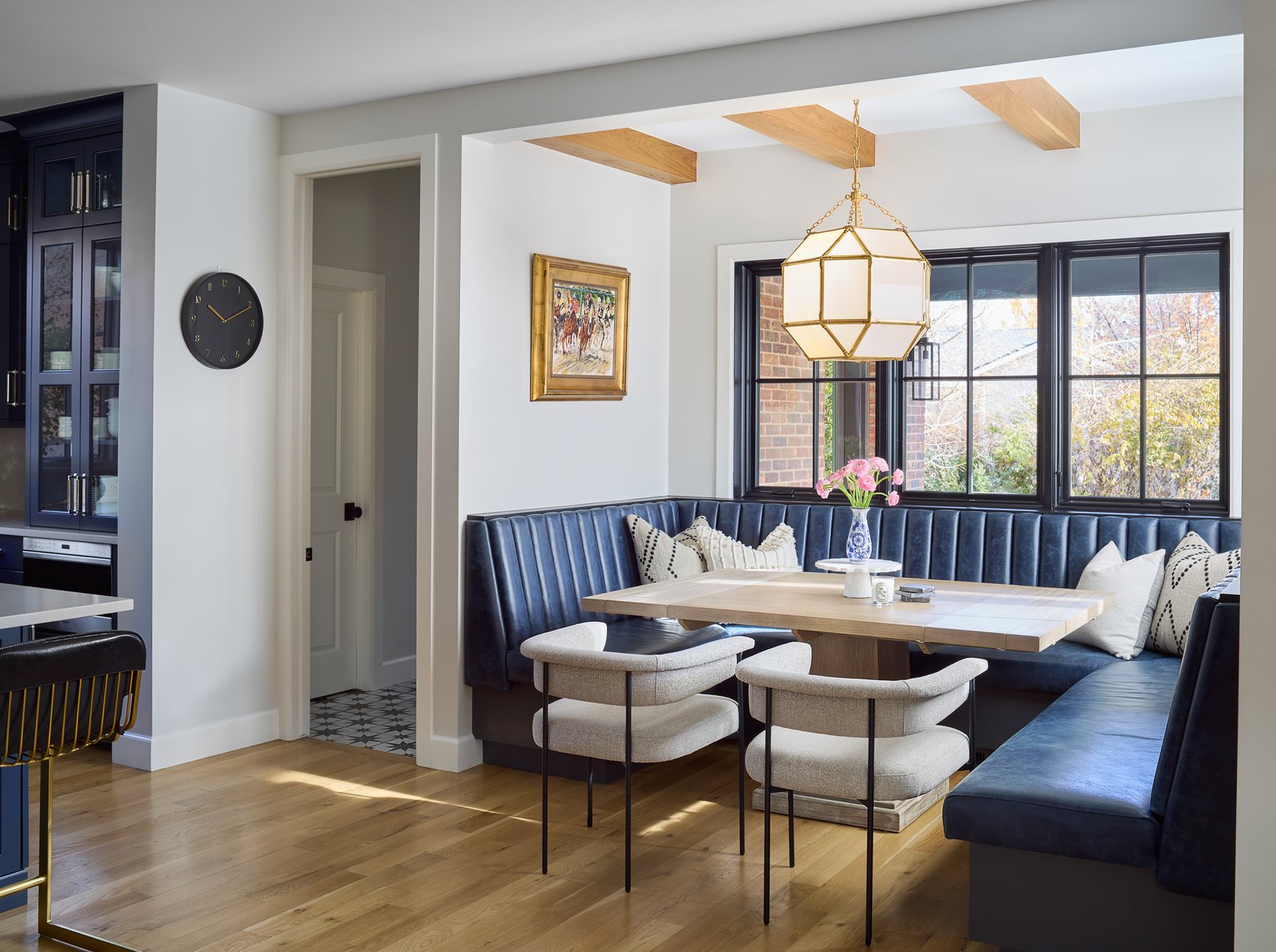 Channel-tufted navy leather banquette under black-framed windows and a brass lantern pendant in the Bonnie Brae remodel, Denver.
