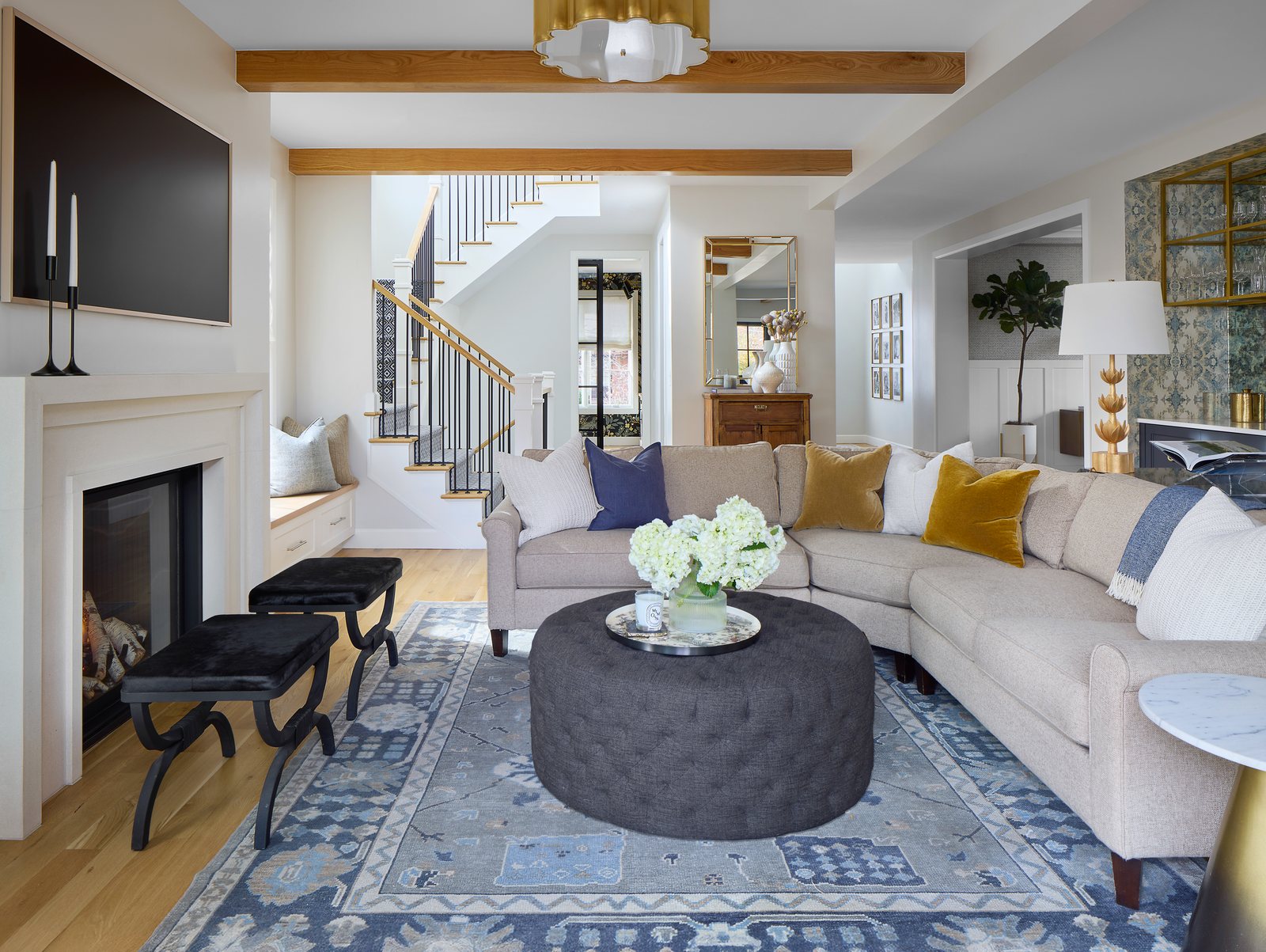 Cream sectional, tufted charcoal ottoman and a blue patterned rug beneath oak beams in the Bonnie Brae living room, Denver.