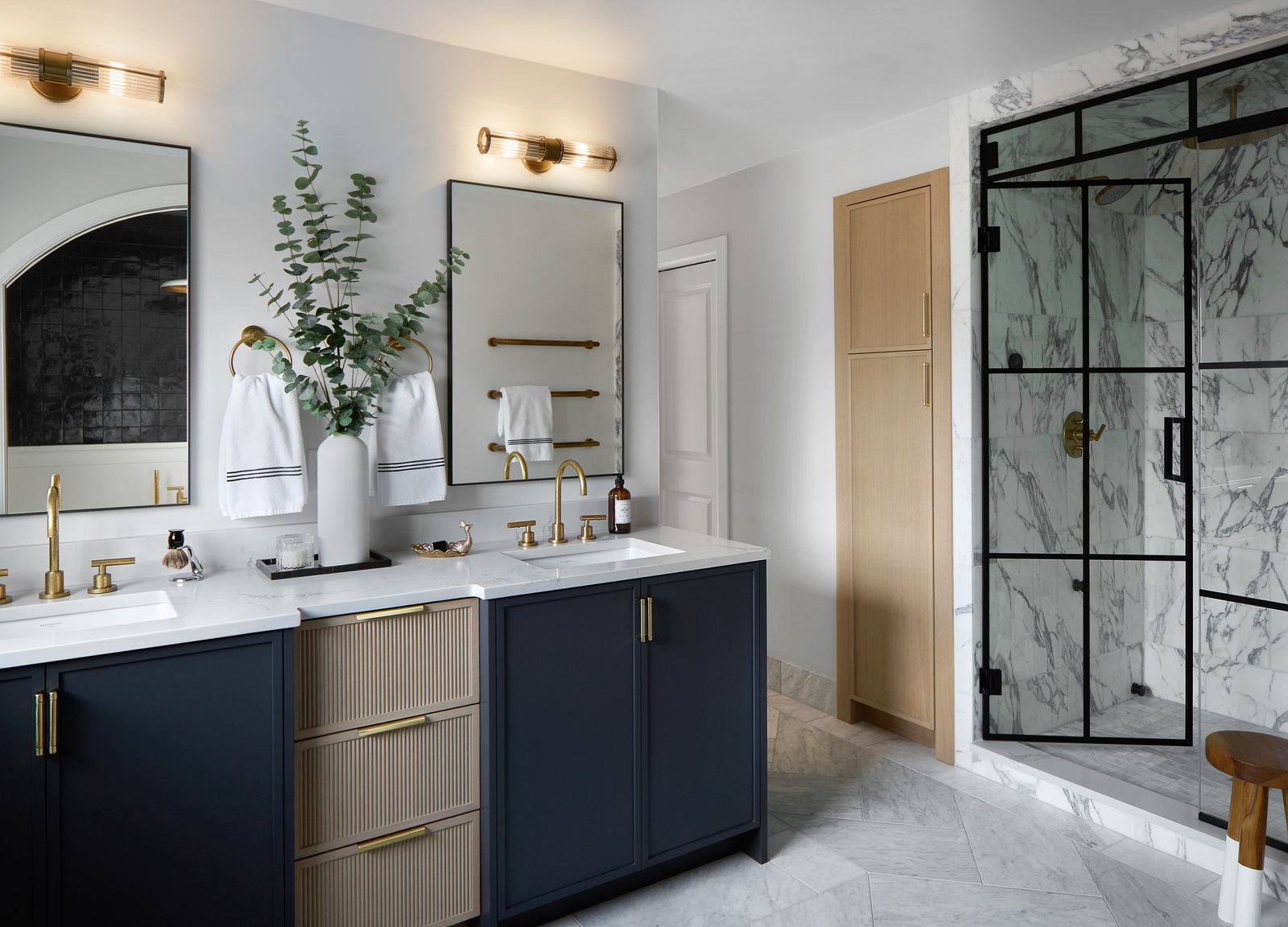 Navy and fluted-oak double vanity with brass fittings beside a black-framed marble shower in the Bonnie Brae primary bathroom, Denver.