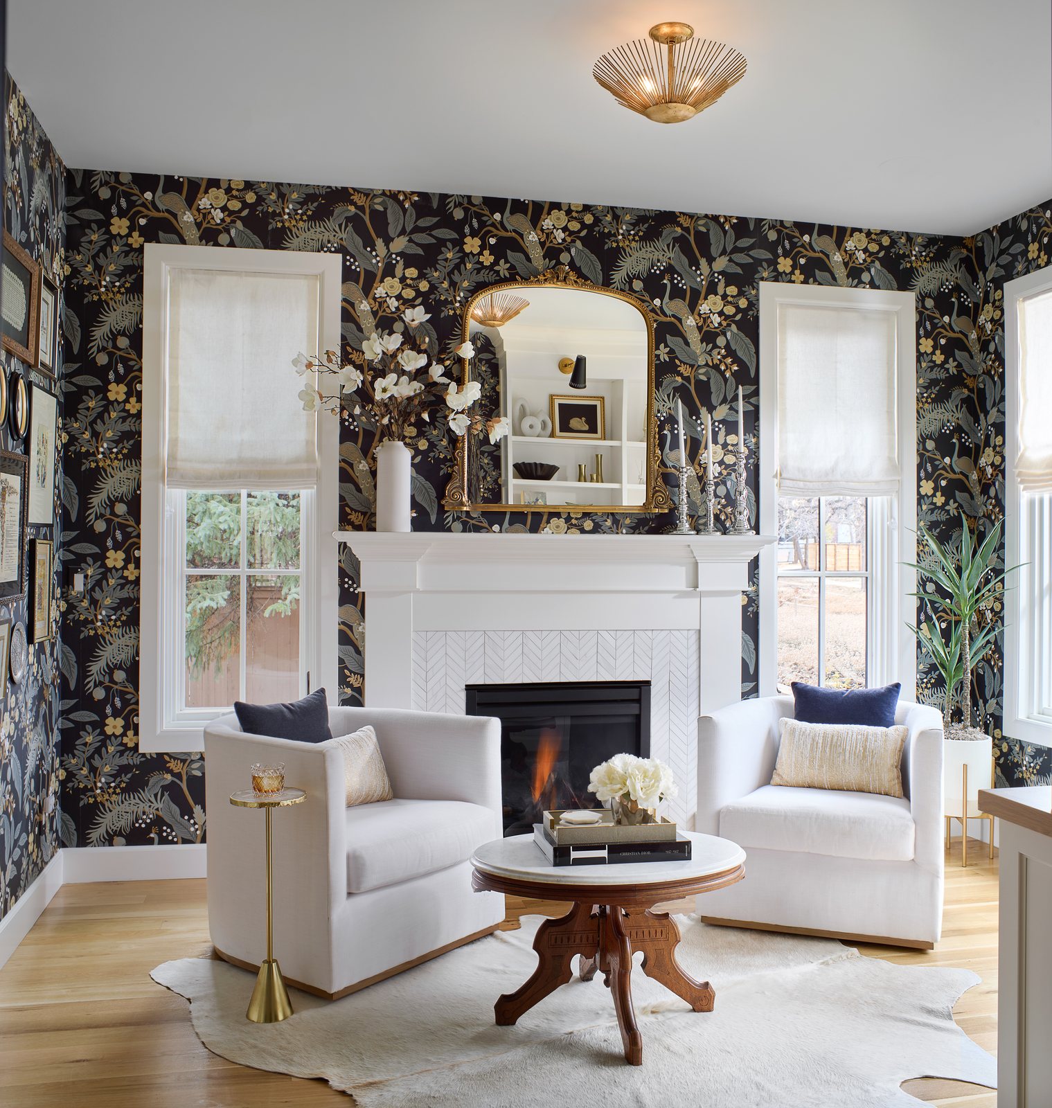 Dark botanical wallpaper, white swivel chairs and a lit fireplace under a gilt mirror in the Bonnie Brae sitting room, Denver.