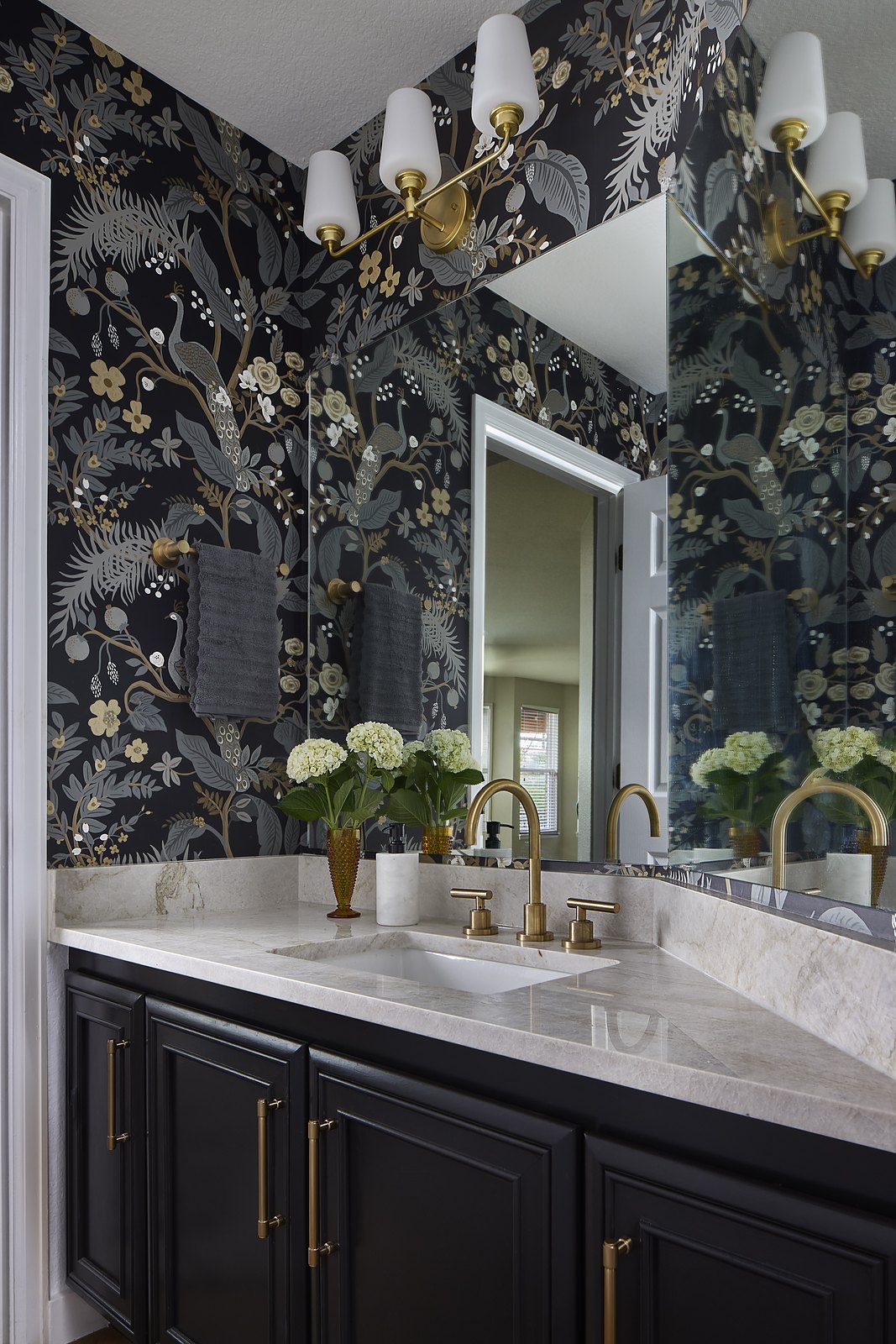 Powder room with dramatic dark botanical wallpaper, a black vanity with brass hardware, a quartzite counter, and double sconces in the Canterberry Crossing remodel in Parker