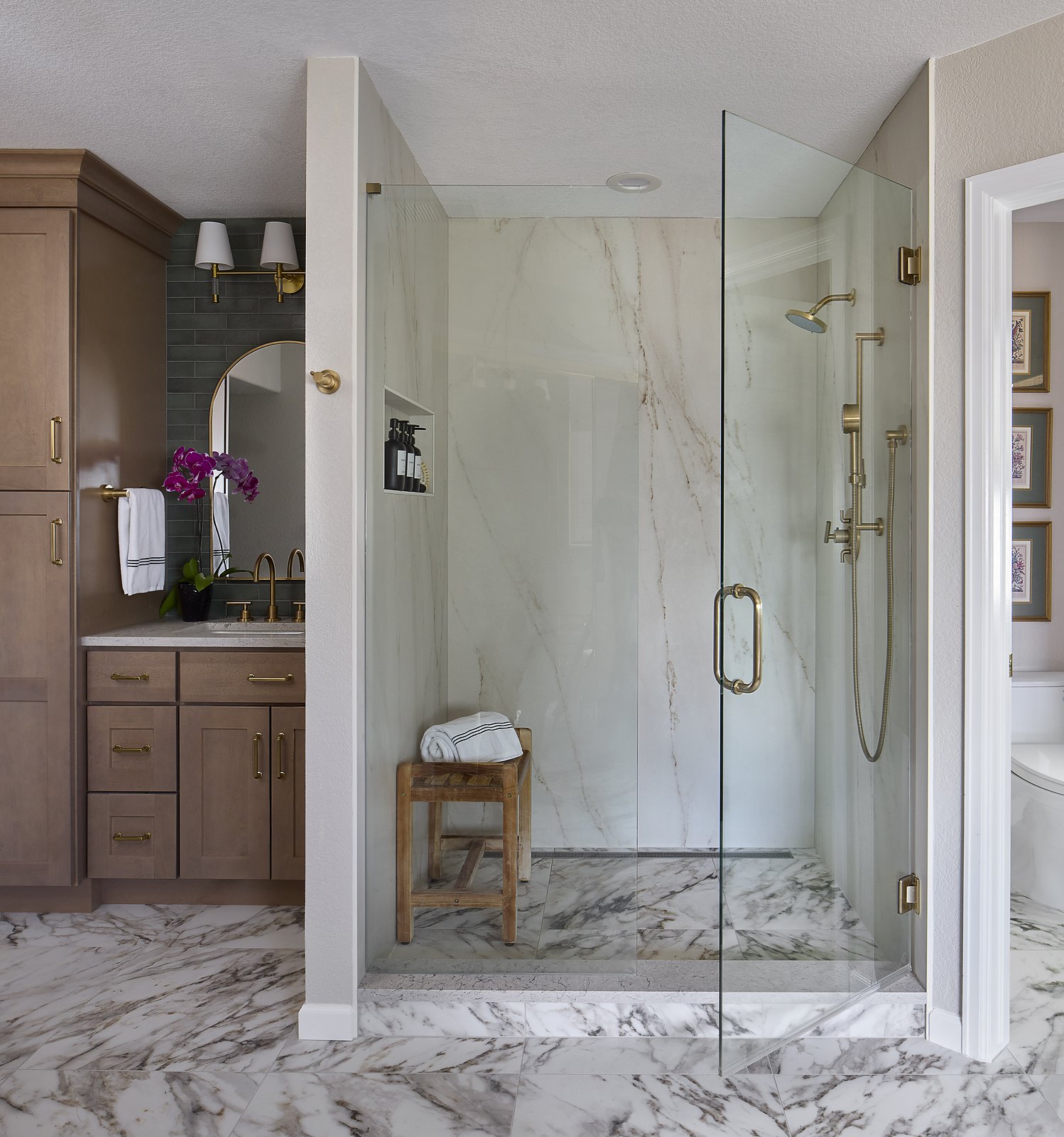 Glass walk-in shower with marble-look slab walls and brass fixtures beside a wood vanity in the Canterberry Crossing primary bathroom, Parker