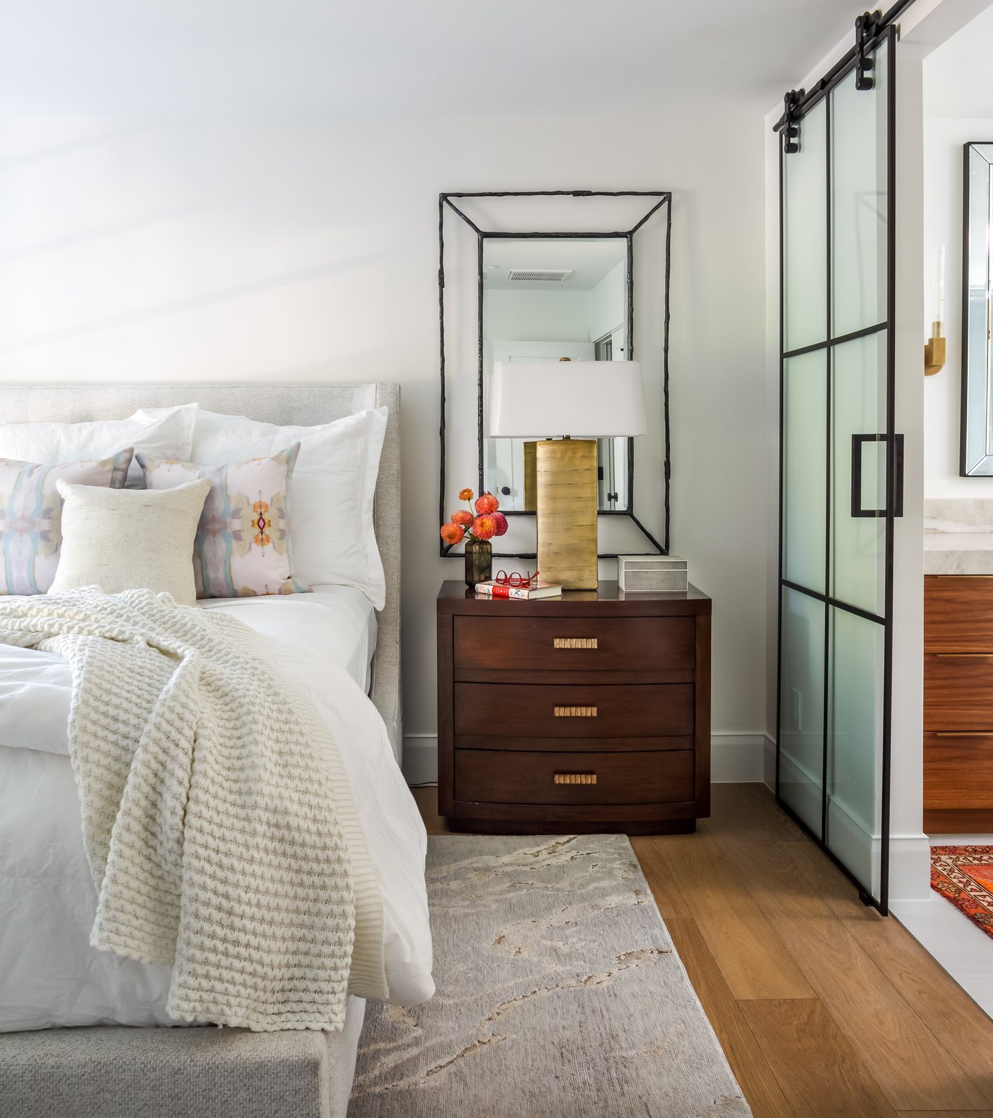 Bedroom with layered white bedding, a walnut nightstand and a black-framed sliding glass door in the Greenwood Village whole-home remodel.