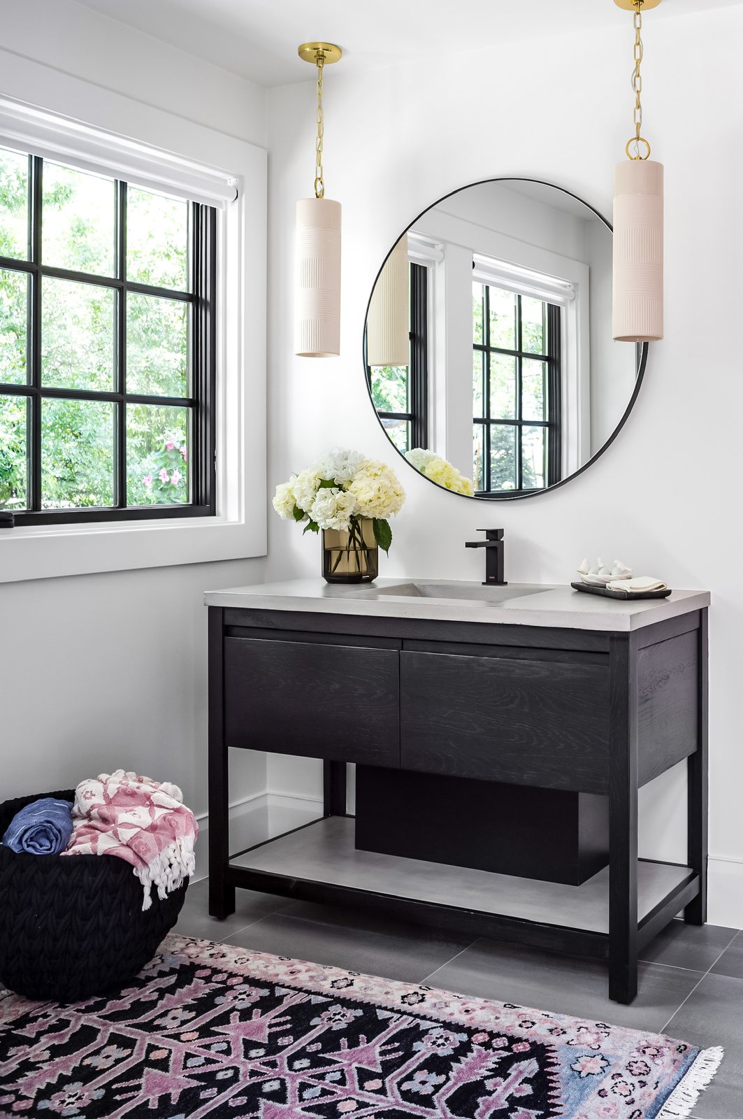 Black vanity with a round mirror, blush pendant and patterned rug in a bathroom of the Greenwood Village whole-home remodel.