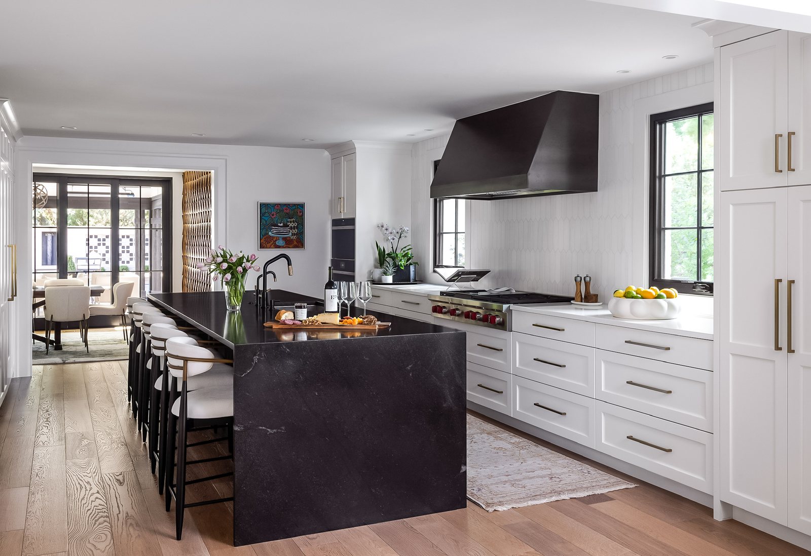 Black stone waterfall island with white perimeter cabinetry and a black range hood in the Greenwood Village whole home remodel kitchen