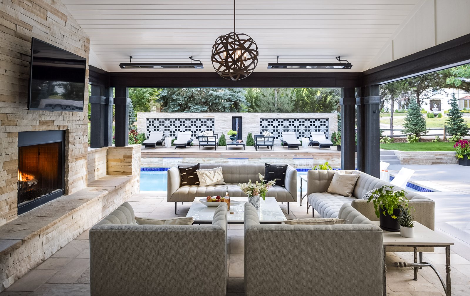 Covered outdoor living room with a stone fireplace and tufted sofas overlooking the pool in the Greenwood Village whole-home remodel.