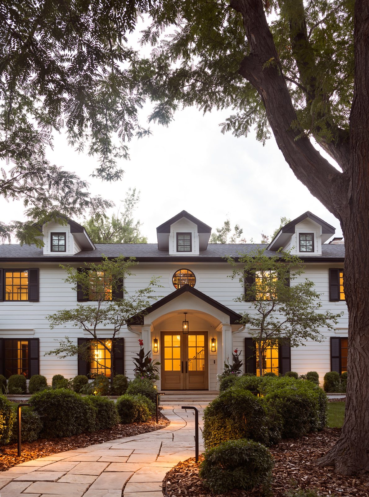Stone walkway leading to the arched front portico and lit double doors of the Greenwood Village whole-home remodel at dusk.