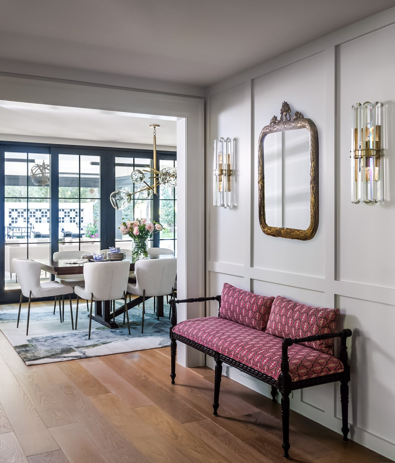 Pink patterned bench and antique mirror in a paneled hallway leading to the dining room in the Greenwood Village whole-home remodel.