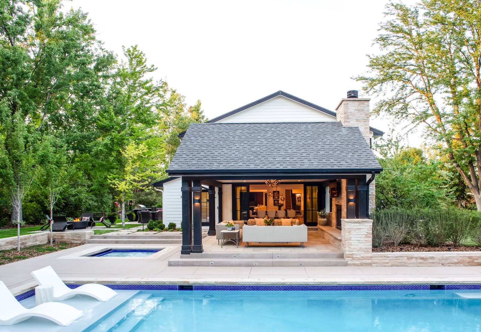 Pool house with a stacked-stone chimney and furnished lounge glowing across the pool and spa at the Greenwood Village whole-home remodel.
