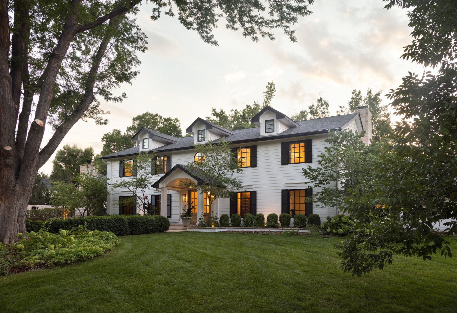 White two-story home with black-shuttered windows glowing at dusk in the Greenwood Village whole-home remodel, Colorado.