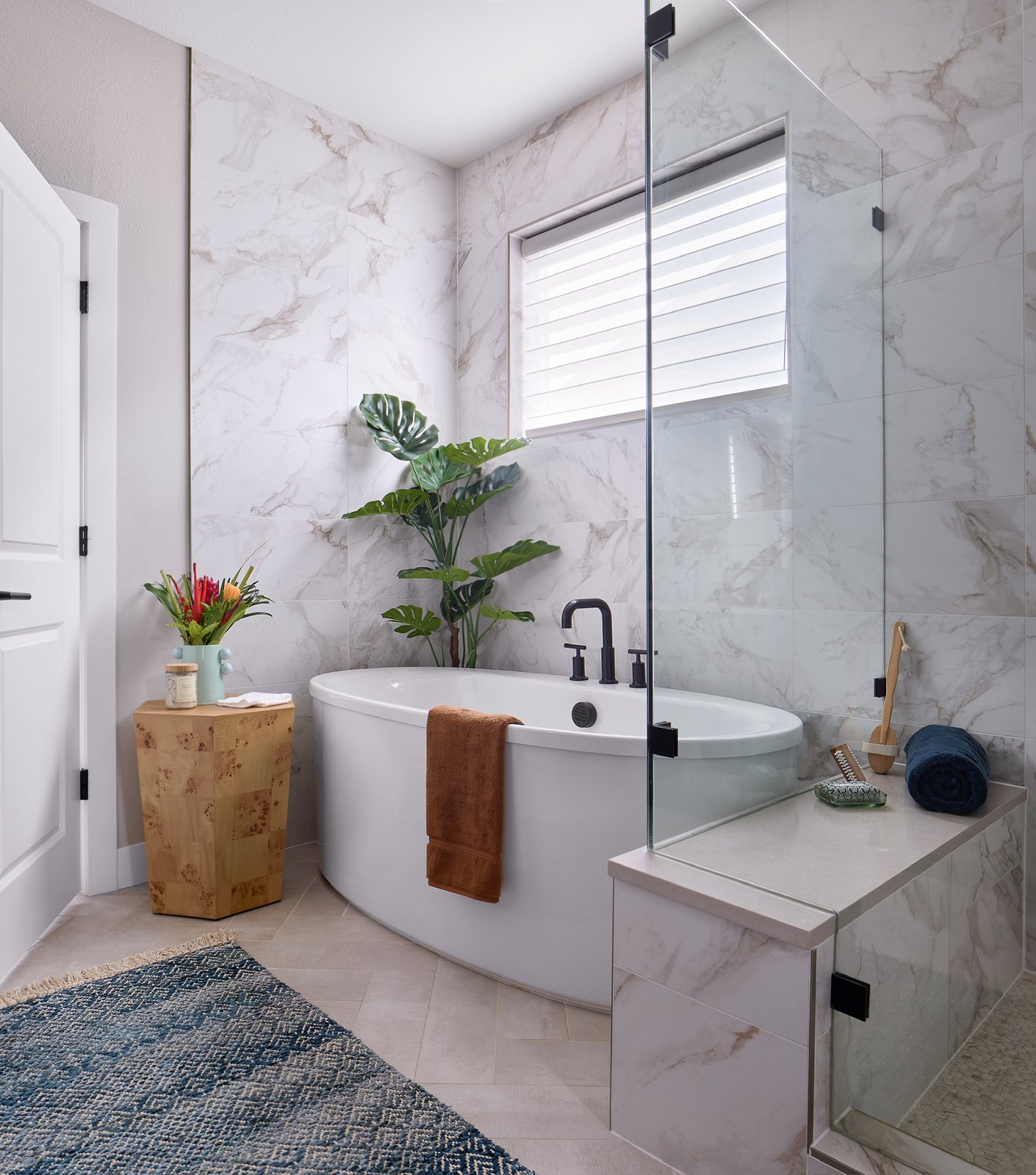 Freestanding oval tub with matte-black filler, marble-look tile and a burl side table in The Canyons new build, Castle Pines.