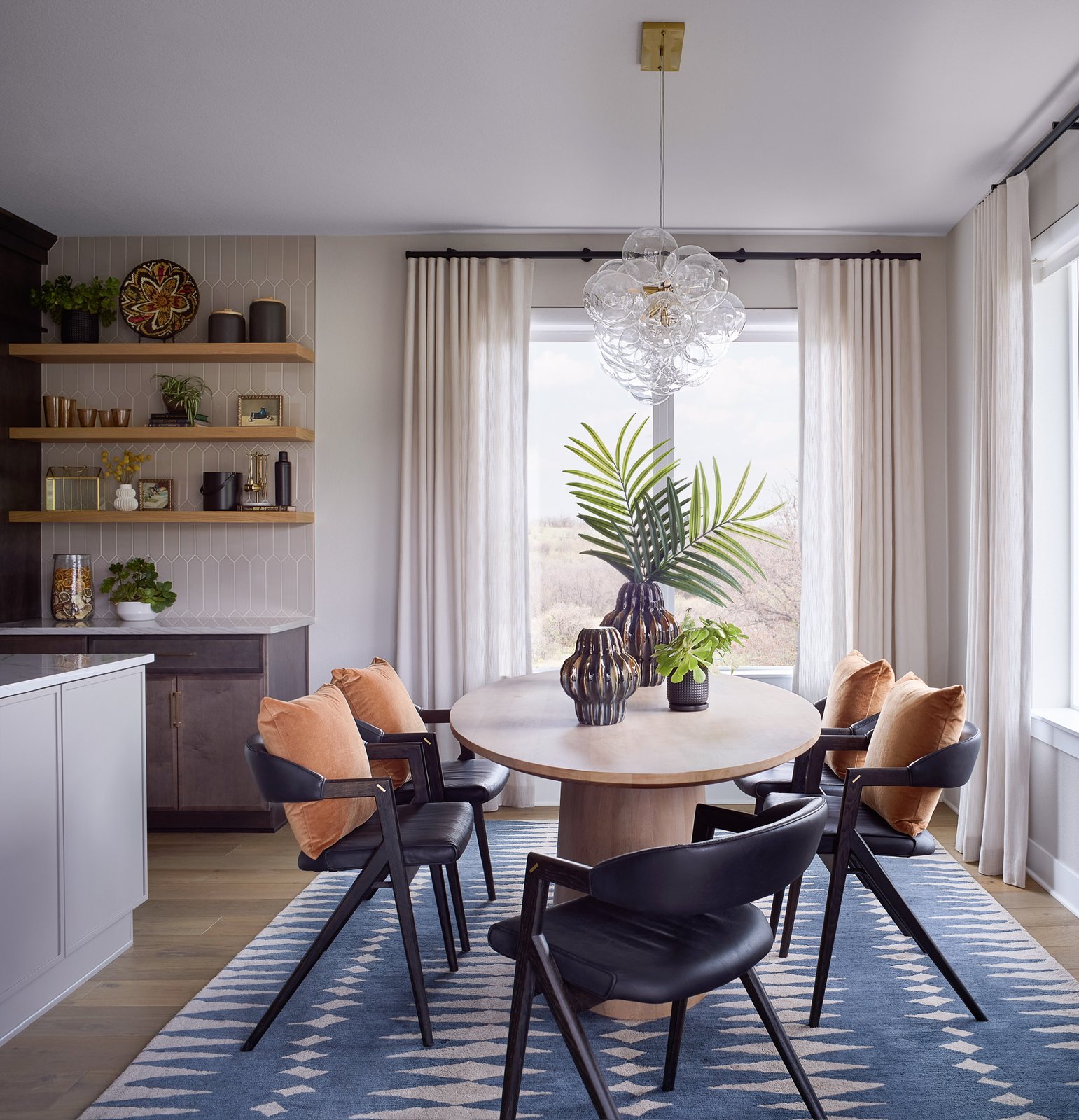 Breakfast nook with a round oak pedestal table, black sculptural chairs and a bubble chandelier in The Canyons new build, Castle Pines.