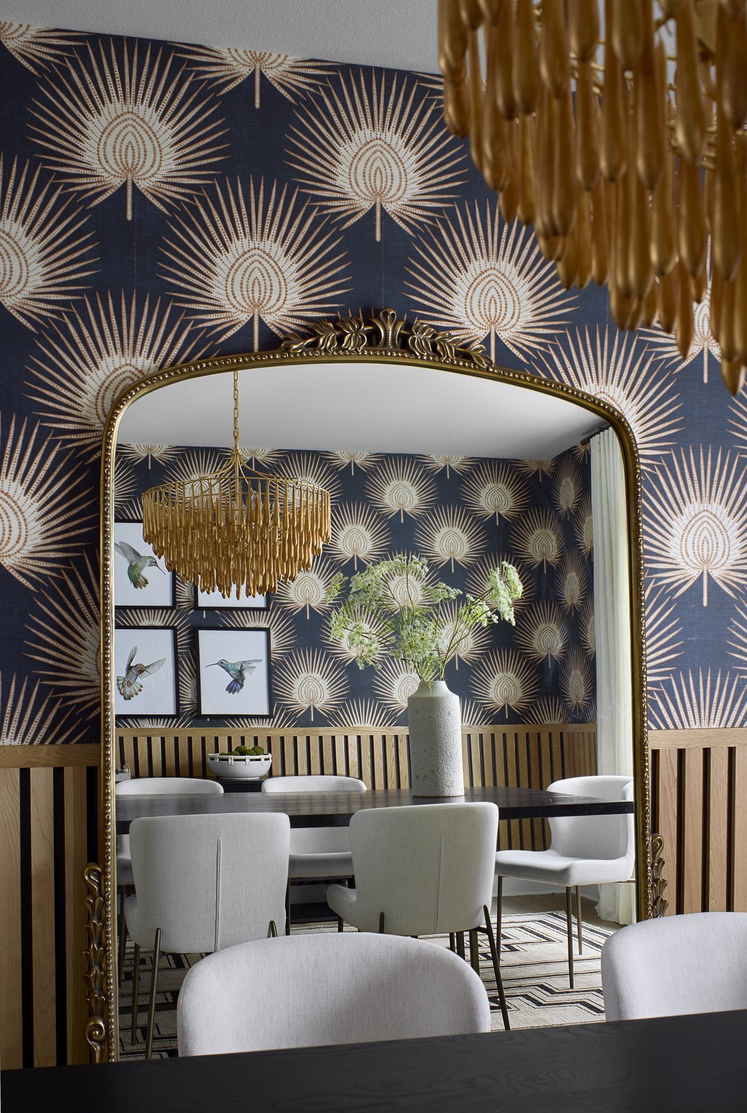 Ornate brass mirror reflecting the dining table and beaded chandelier against fan-motif wallpaper in The Canyons dining room, Castle Pines.