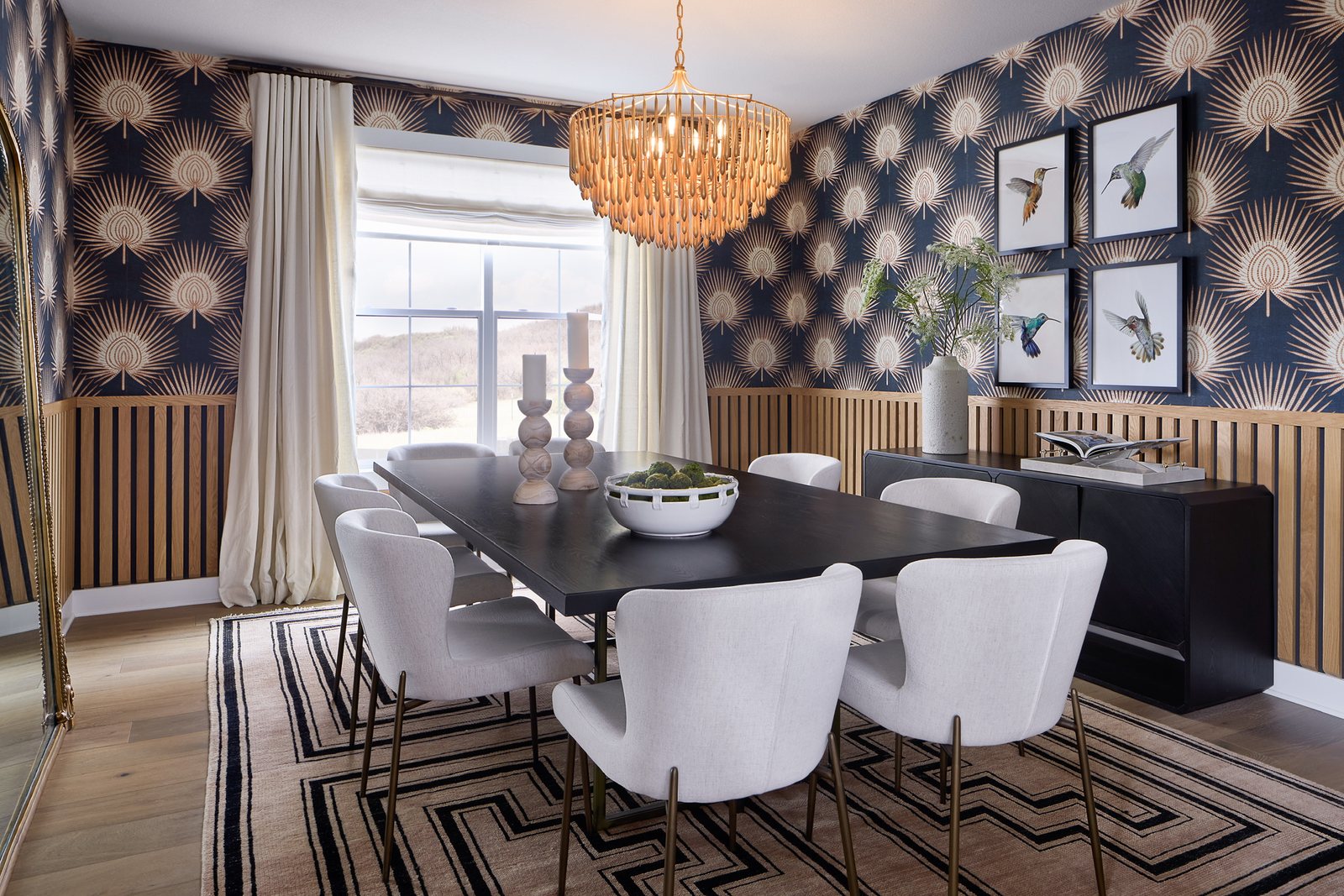Dining room with navy fan-motif wallpaper, oak slat wainscoting, black table and lit beaded chandelier in The Canyons new build, Castle Pines.