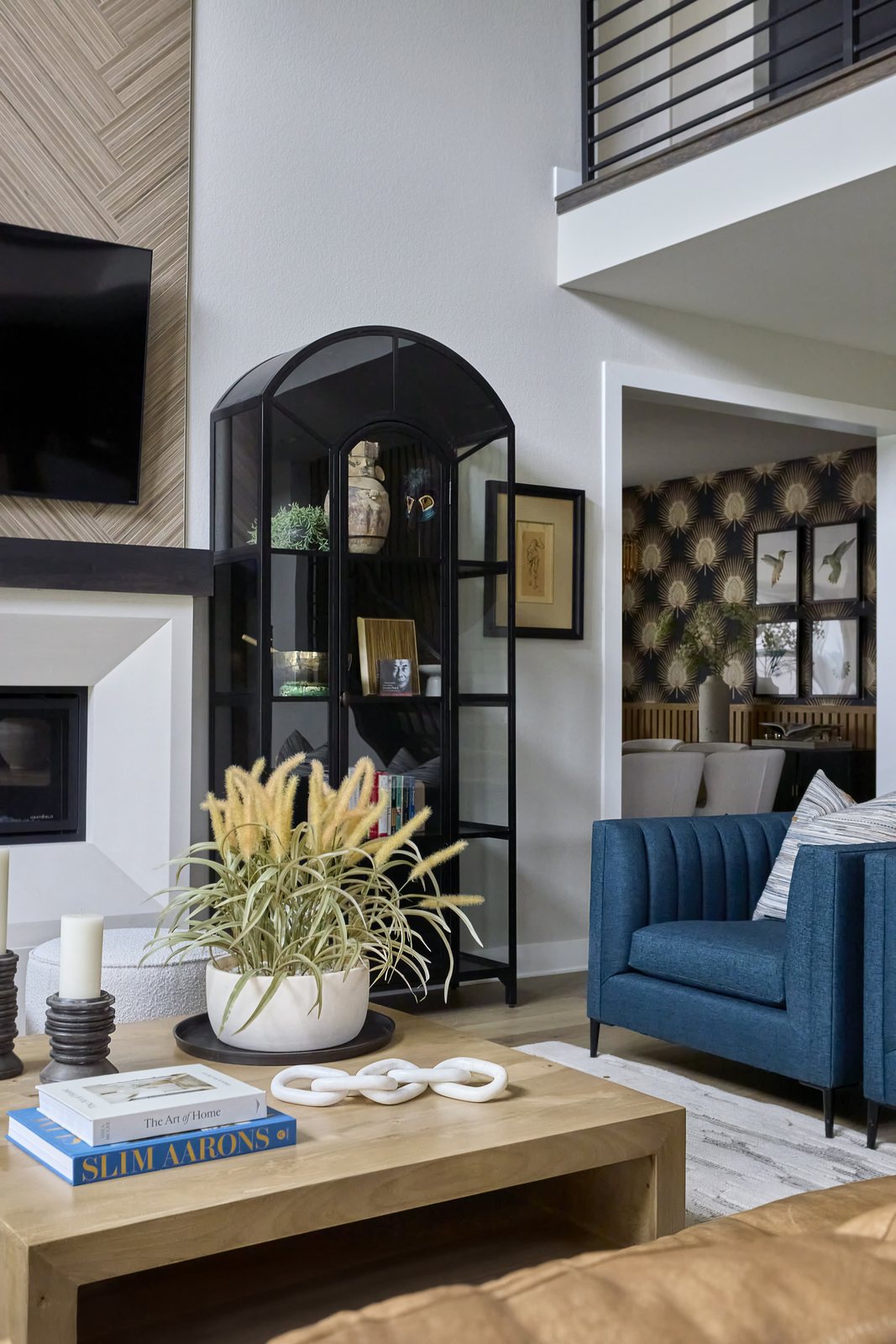 An arched black display cabinet and blue channel-tufted armchair frame the view from the great room into the wallpapered dining room in The Canyons new build, Castle Pines.