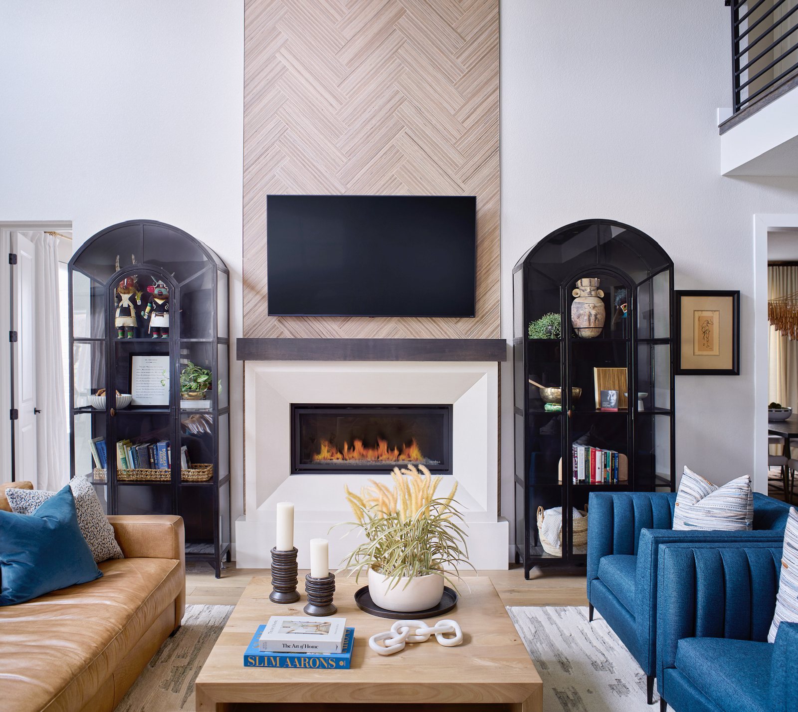 Herringbone-tile fireplace flanked by arched black display cabinets and blue armchairs in The Canyons new build, Castle Pines.