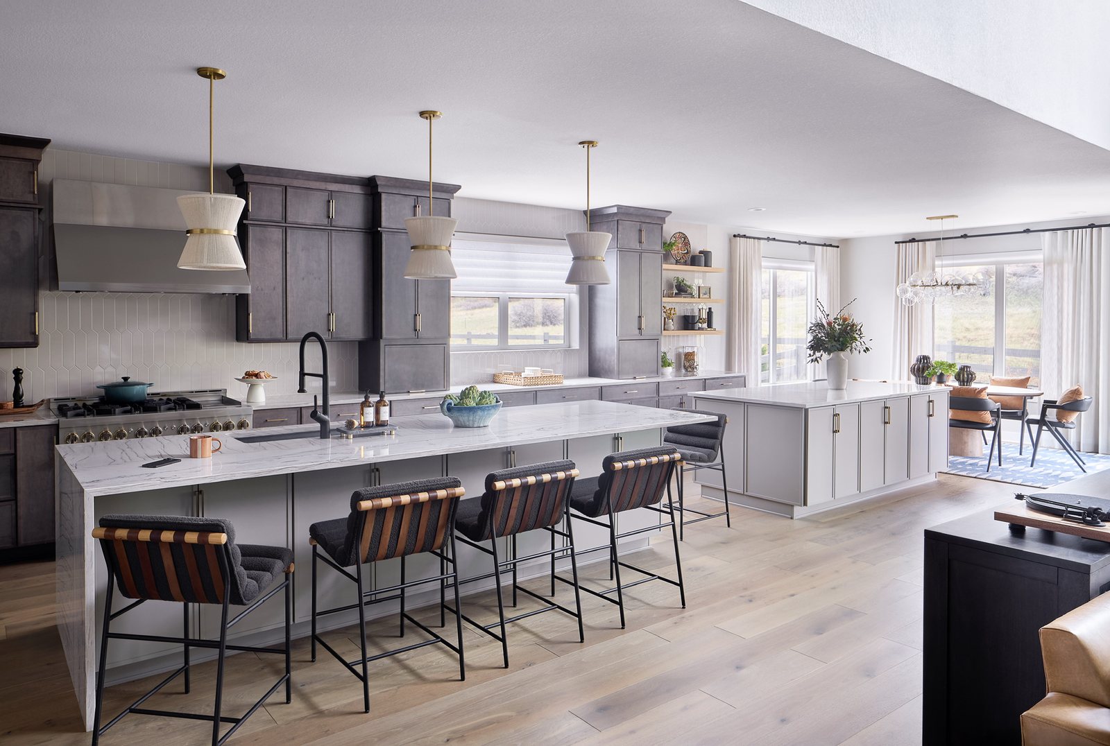 Double-island kitchen with gray-stained cabinetry, marble waterfall counters and leather-strap stools in The Canyons new build, Castle Pines.