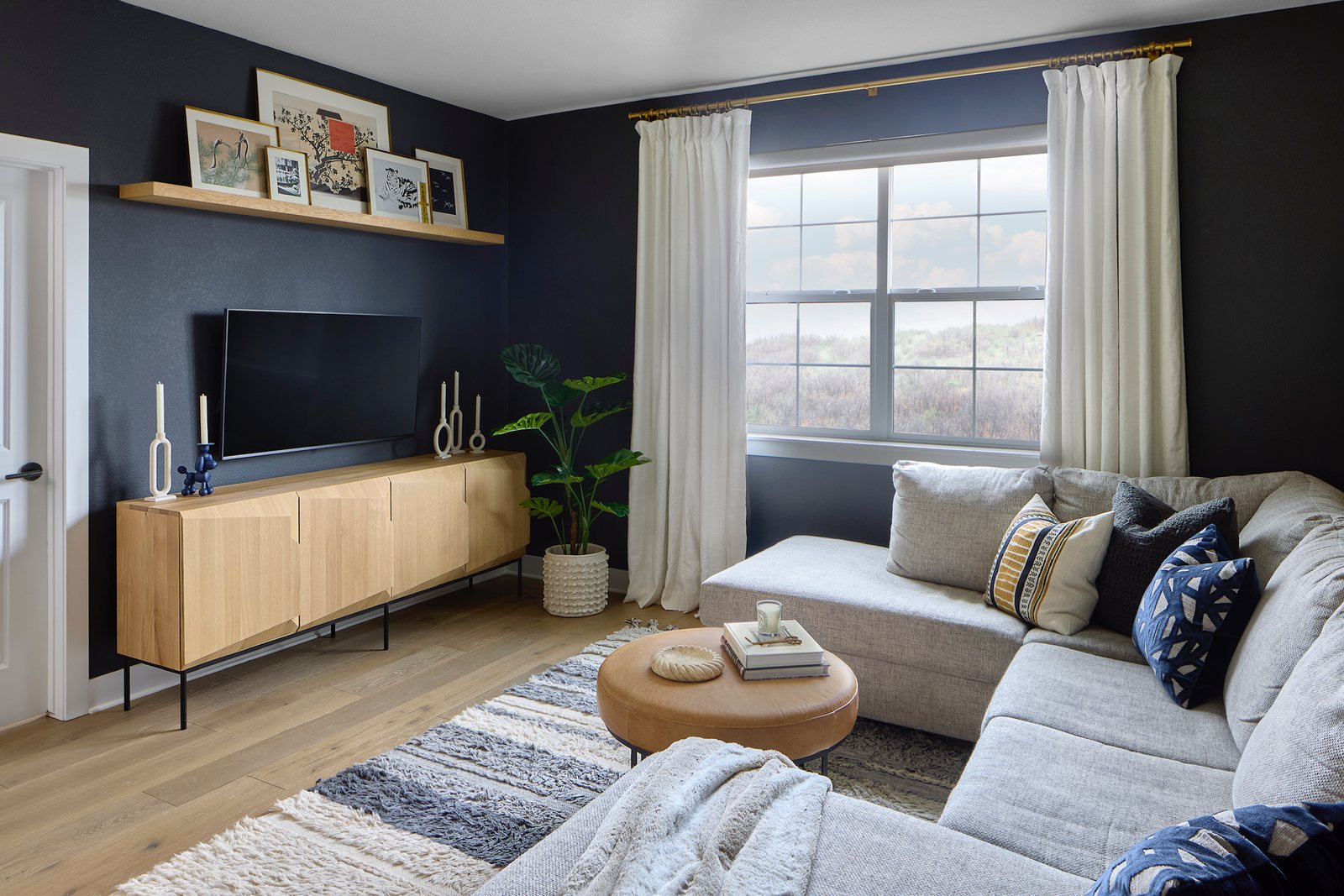 Media lounge with a black accent wall, oak media cabinet and gray sectional layered with blue pillows in The Canyons new build, Castle Pines.
