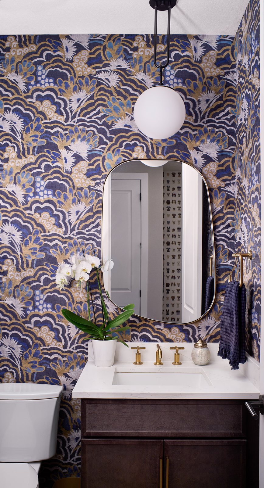 Powder room wrapped in blue-and-gold botanical wallpaper with a brass-trimmed mirror and globe pendant in The Canyons new build, Castle Pines.