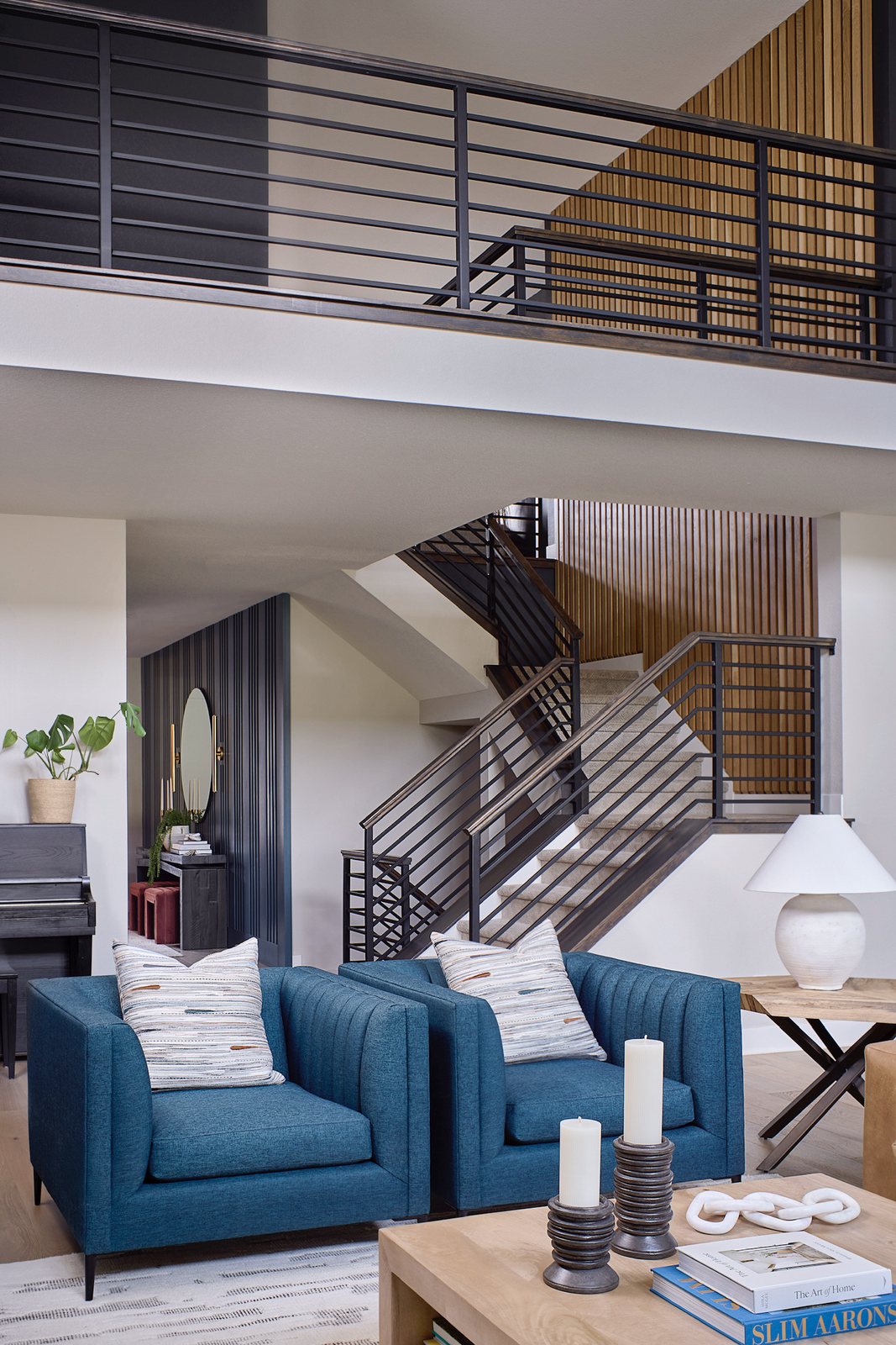 Open steel-railed staircase with an oak slat feature wall rising behind blue armchairs in The Canyons new build, Castle Pines.