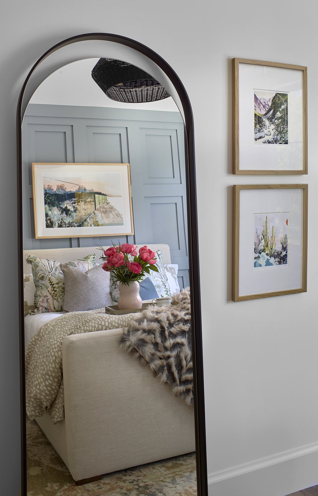 An arched floor mirror reflects the styled bed in the Washington Park showhouse bedroom in Denver, beside two framed desert prints in oak frames.