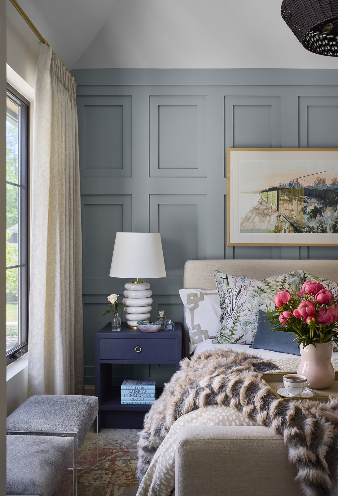 Bedside vignette in the Washington Park showhouse bedroom in Denver, with a navy nightstand, sculptural lamp, and coral peonies beside layered pillows.
