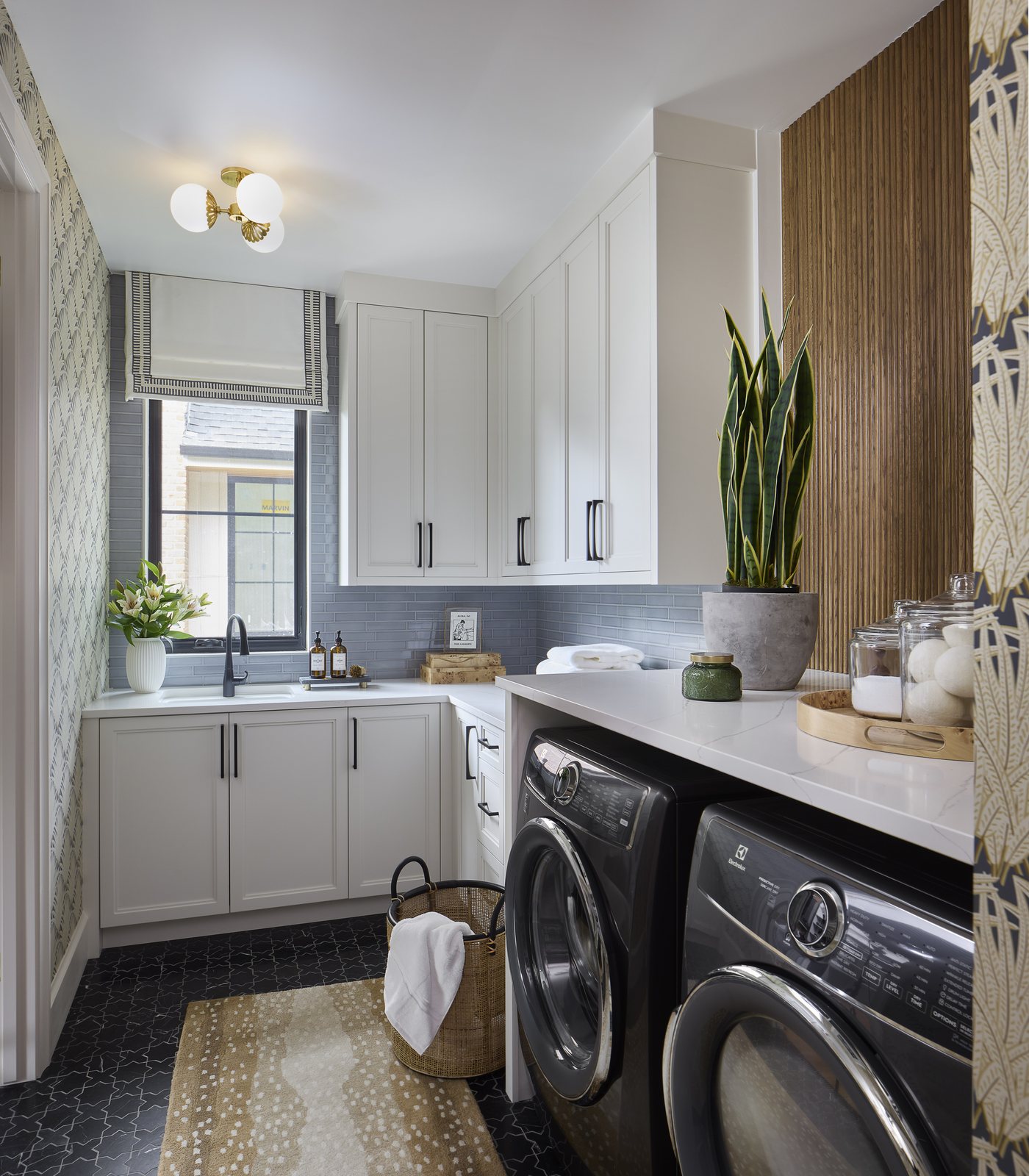 The laundry room of the Washington Park showhouse in Denver, with white cabinetry, blue glass tile, a fluted wood slat wall, and black washer and dryer under a quartz counter.