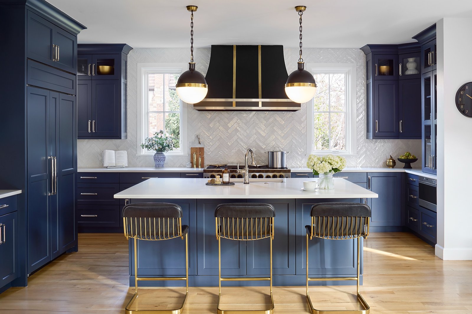 Navy kitchen with white herringbone backsplash and brass barstools after the whole house remodel