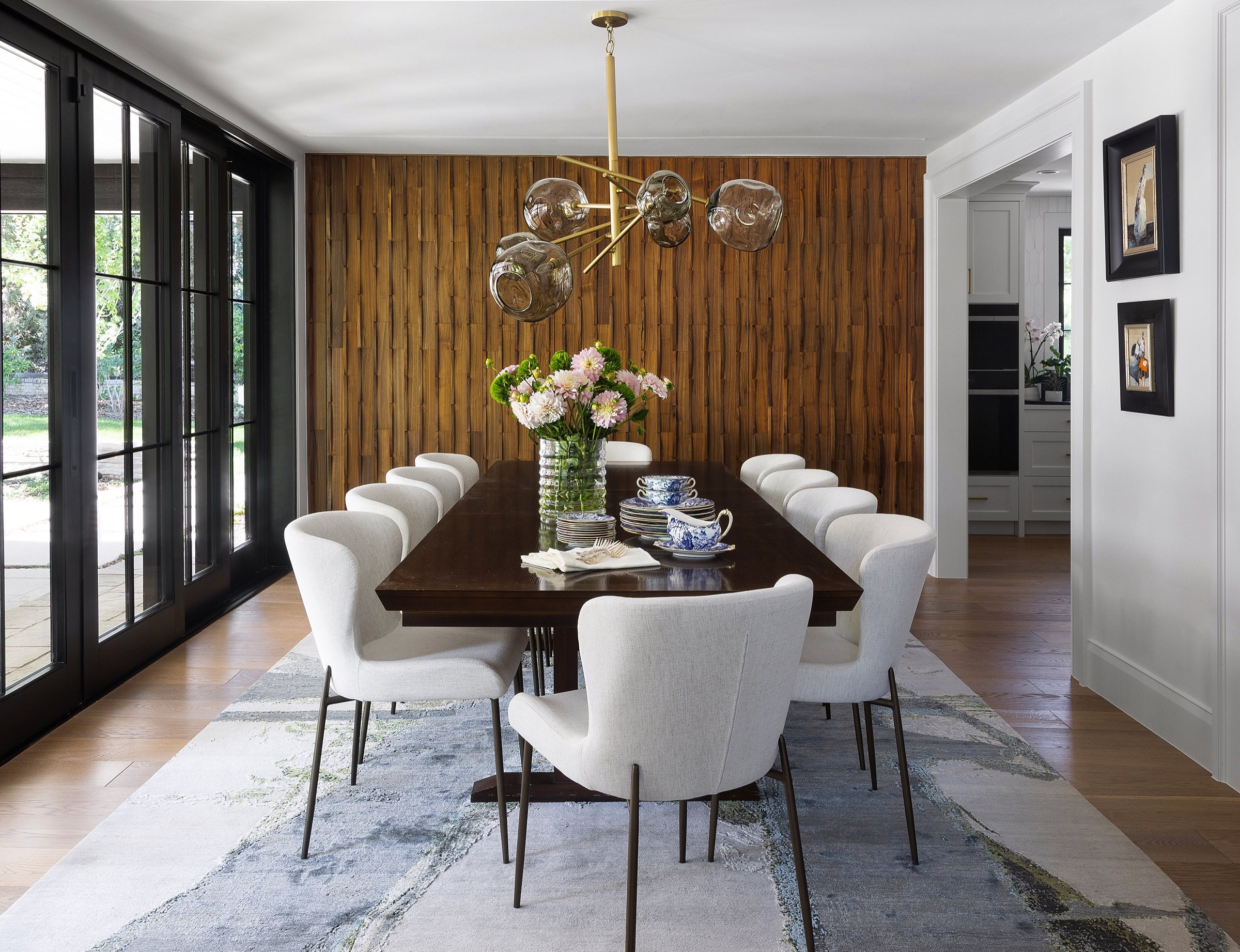 Dining room with seamless wood-paneled wall, white chairs, and organic rug in the Greenwood Village whole home renovation