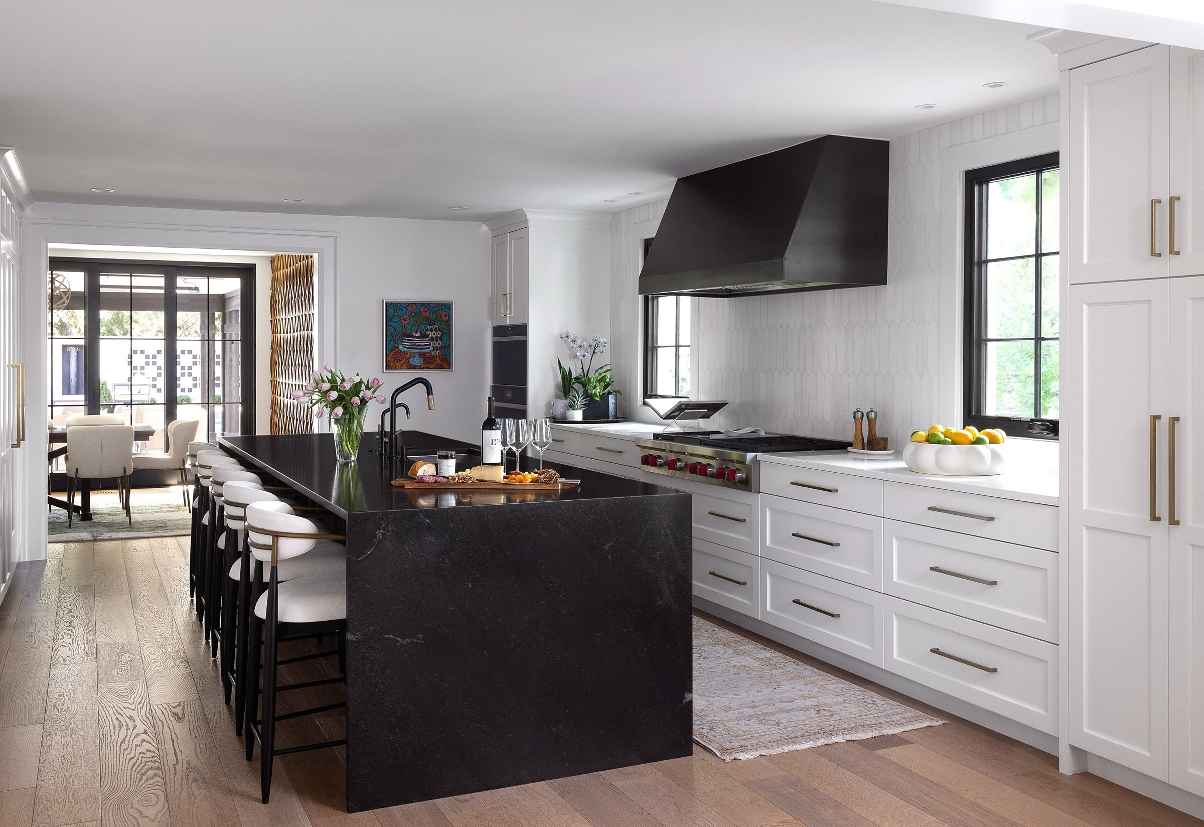 Modern kitchen with white perimeter cabinets, black metal freestanding hood, and black waterfall island with gold hardware