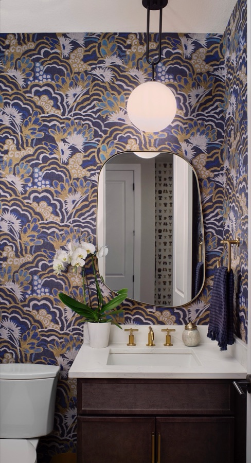 Powder bathroom with blue and gold patterned wallpaper, oval mirror, brass faucet, and dark vanity in The Canyons at Castle Pines