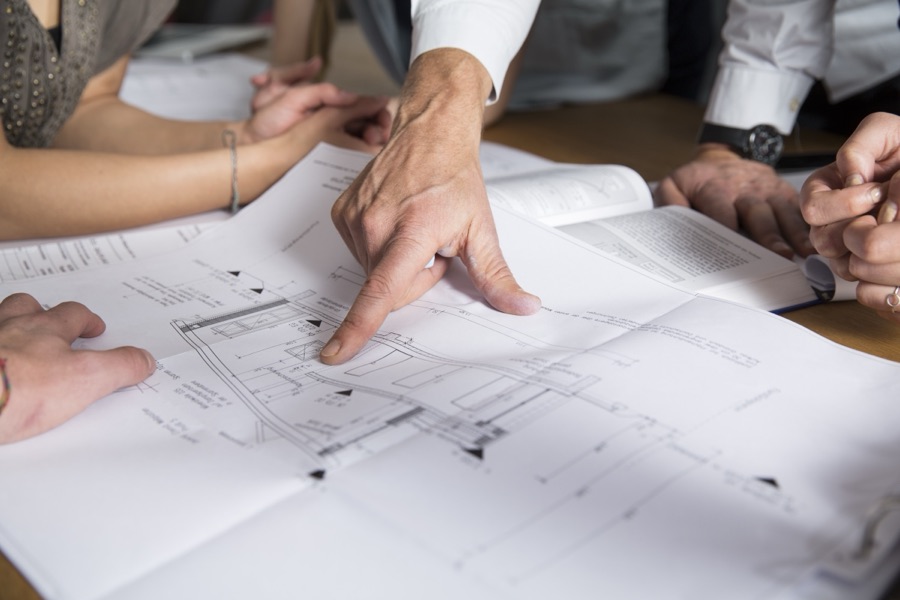 Design team reviewing architectural drawings and construction documents by hand during a new construction planning meeting